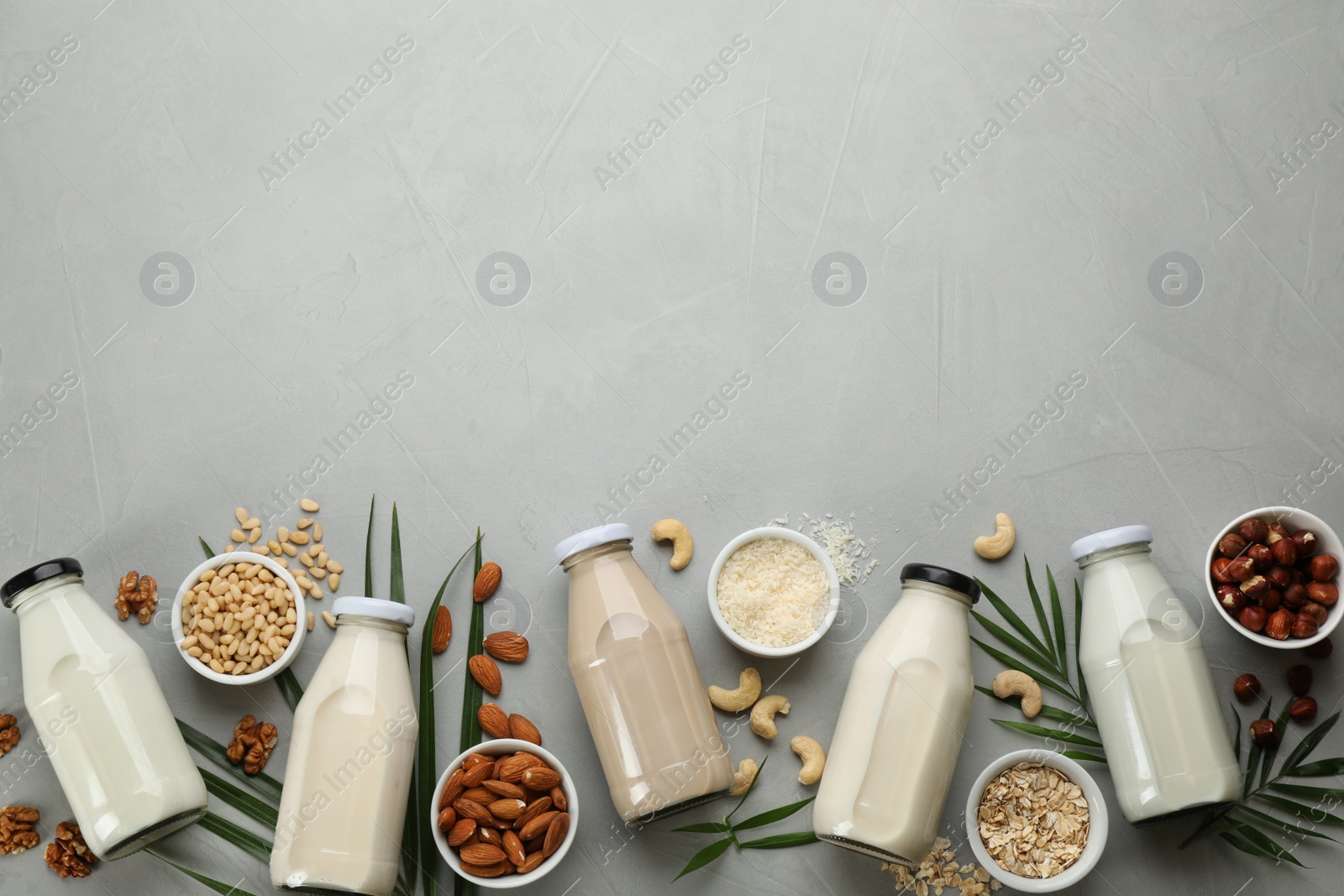 Photo of Different vegan milks and ingredients on light grey table, flat lay. Space for text