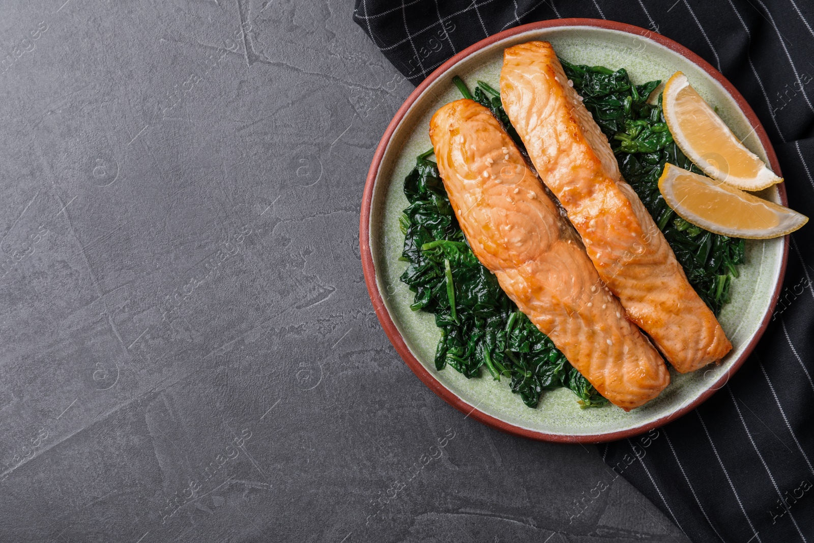 Photo of Tasty salmon with spinach and lemon on grey table, flat lay. Space for text