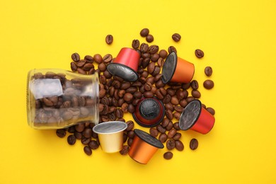 Many coffee capsules, beans and glass jar on yellow background, flat lay