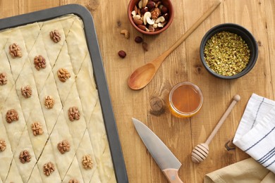 Photo of Making delicious baklava. Baking pan with dough and ingredients on wooden table, flat lay
