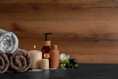 Photo of Beautiful spa composition with different care products and burning candles on black table. Space for text