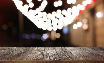 Empty wooden surface and blurred view of night street decorated for Christmas. Bokeh effect