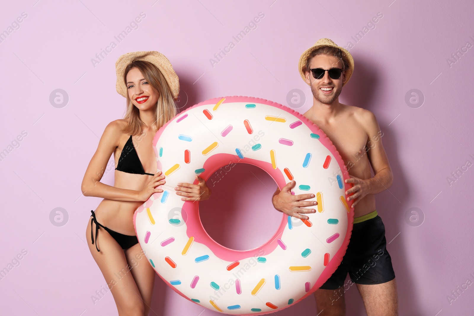 Photo of Happy young couple in beachwear with inflatable ring on color background