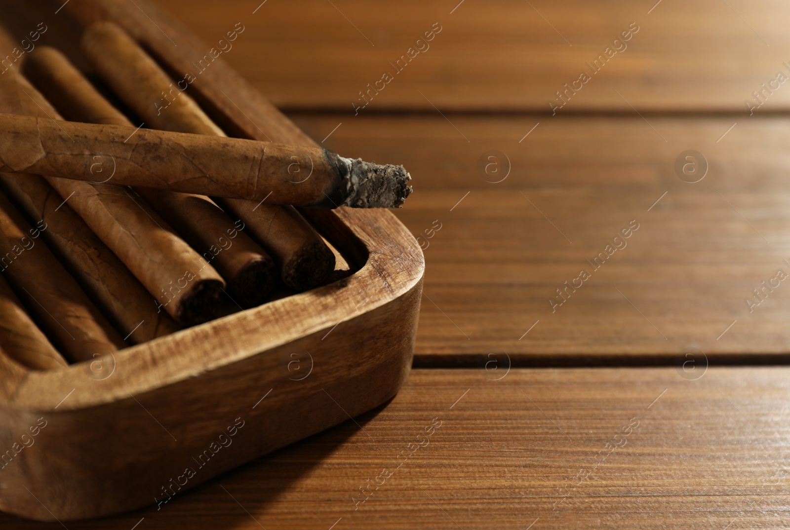 Photo of Many cigars in box on wooden table, closeup. Space for text