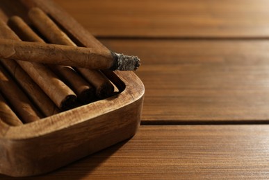 Photo of Many cigars in box on wooden table, closeup. Space for text