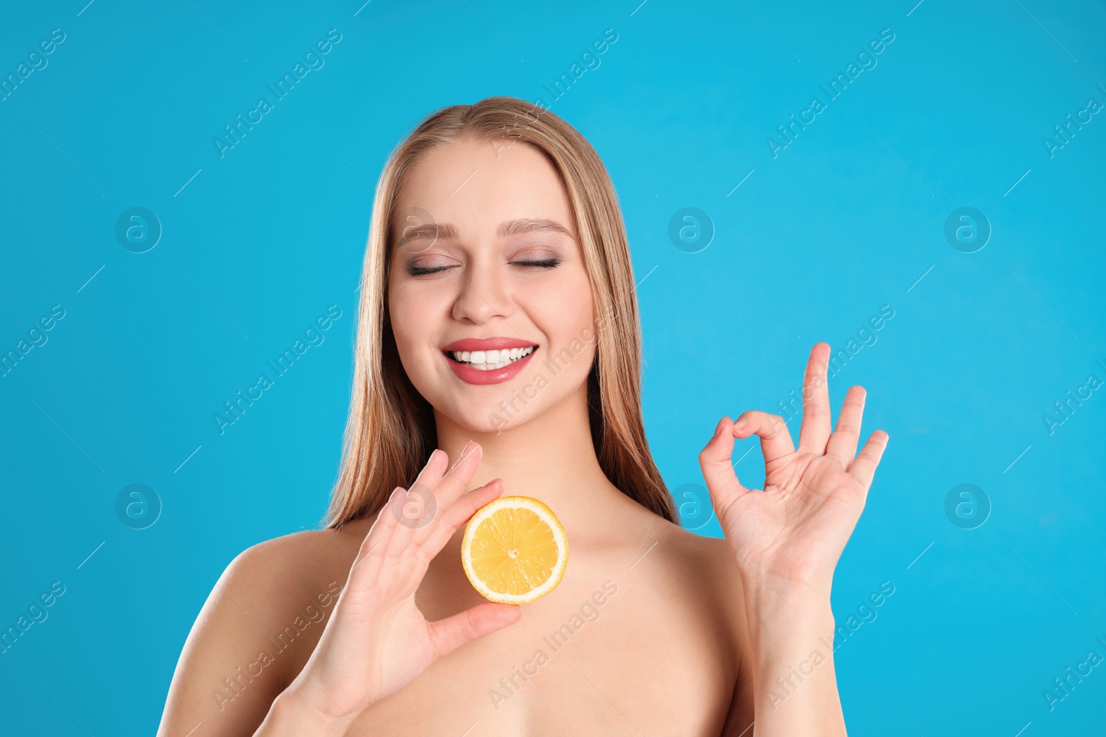 Photo of Young woman with cut lemon on blue background. Vitamin rich food