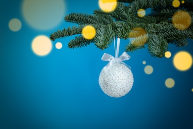 Photo of Beautiful Christmas ball hanging on fir tree branch against light blue background, bokeh effect. Space for text