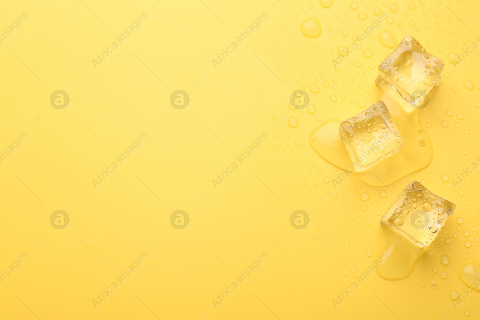 Photo of Crystal clear ice cubes on yellow background, flat lay. Space for text