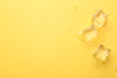 Crystal clear ice cubes on yellow background, flat lay. Space for text