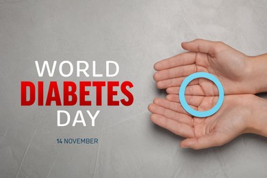 Image of World Diabetes Day. Woman holding blue paper circle at grey table, top view