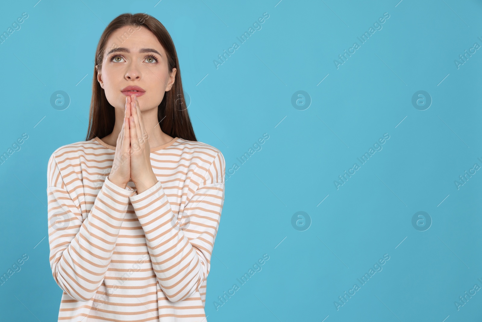 Photo of Woman with clasped hands praying on turquoise background, space for text