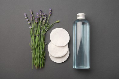 Photo of Bottle of makeup remover, cotton pads and lavender on dark grey background, flat lay