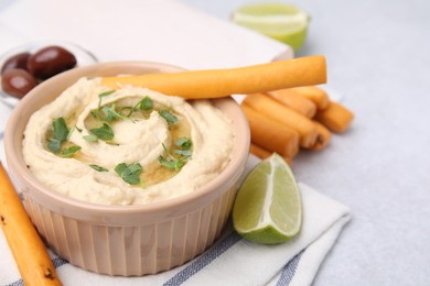 Delicious hummus with grissini sticks on light grey table, closeup