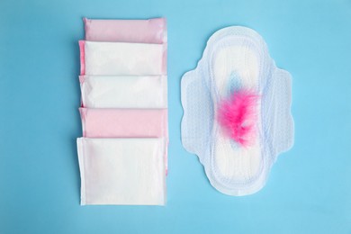 Photo of Menstrual pads and pink feather on light blue background, flat lay