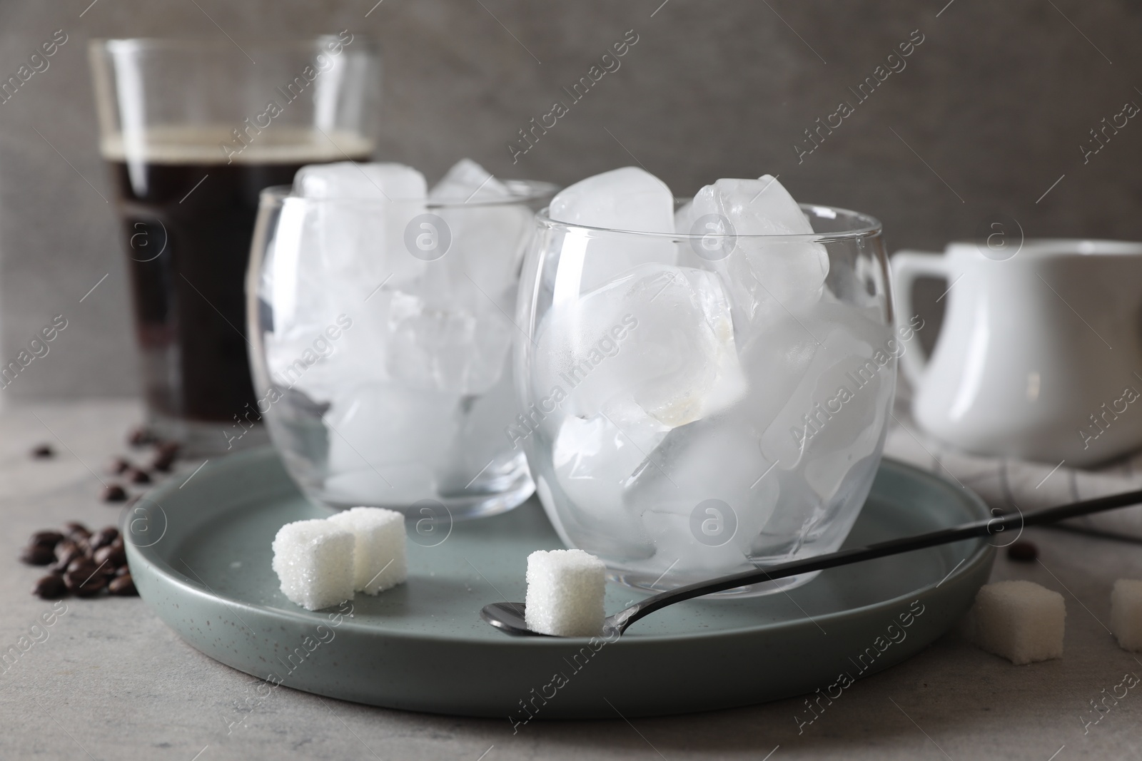 Photo of Making iced coffee. Ice cubes in glasses, ingredients and spoon on gray table, closeup