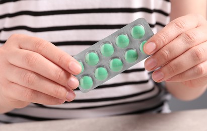 Photo of Woman with blister of green pills at grey table, closeup