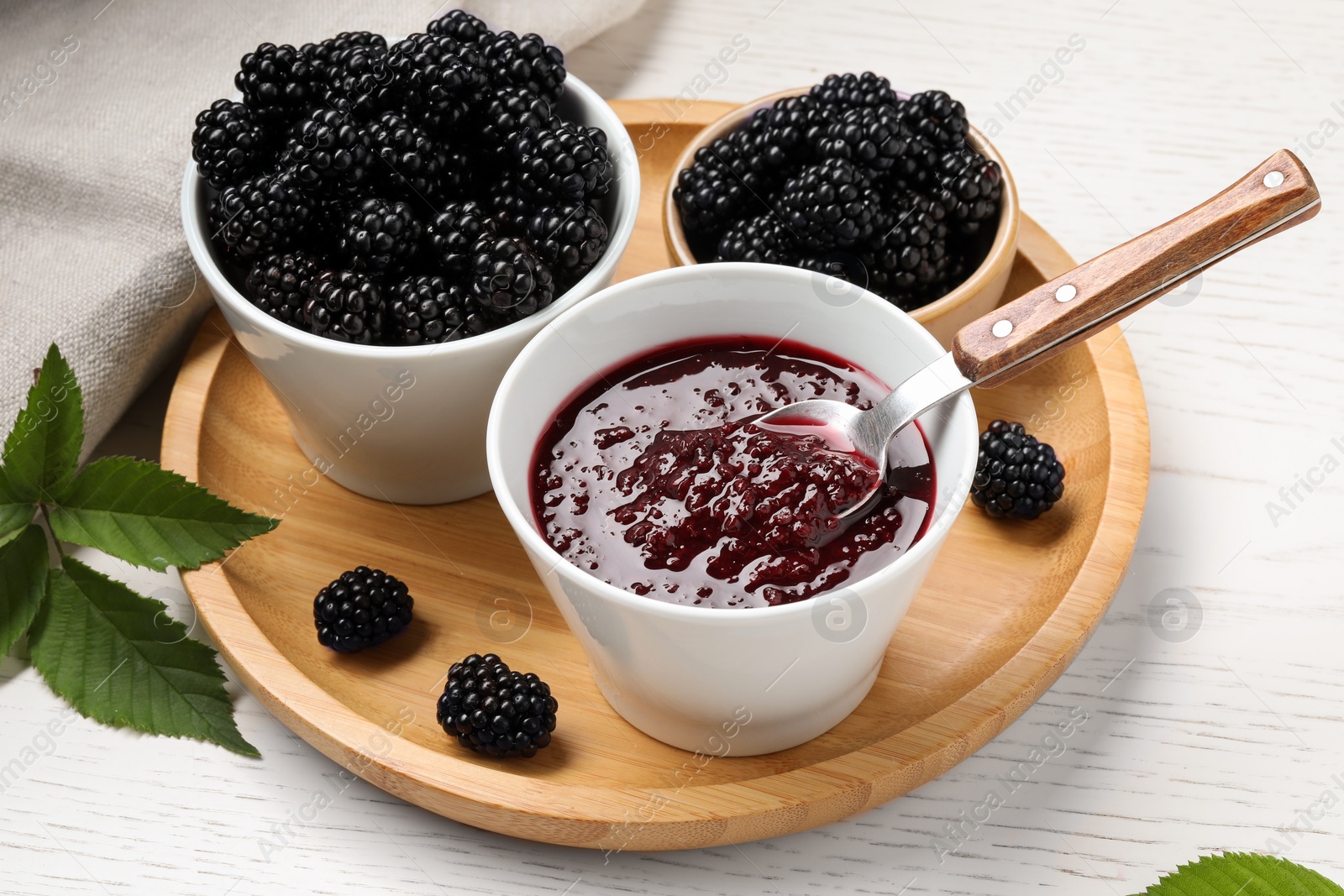 Photo of Fresh ripe blackberries, tasty jam and leaves on white wooden table, closeup