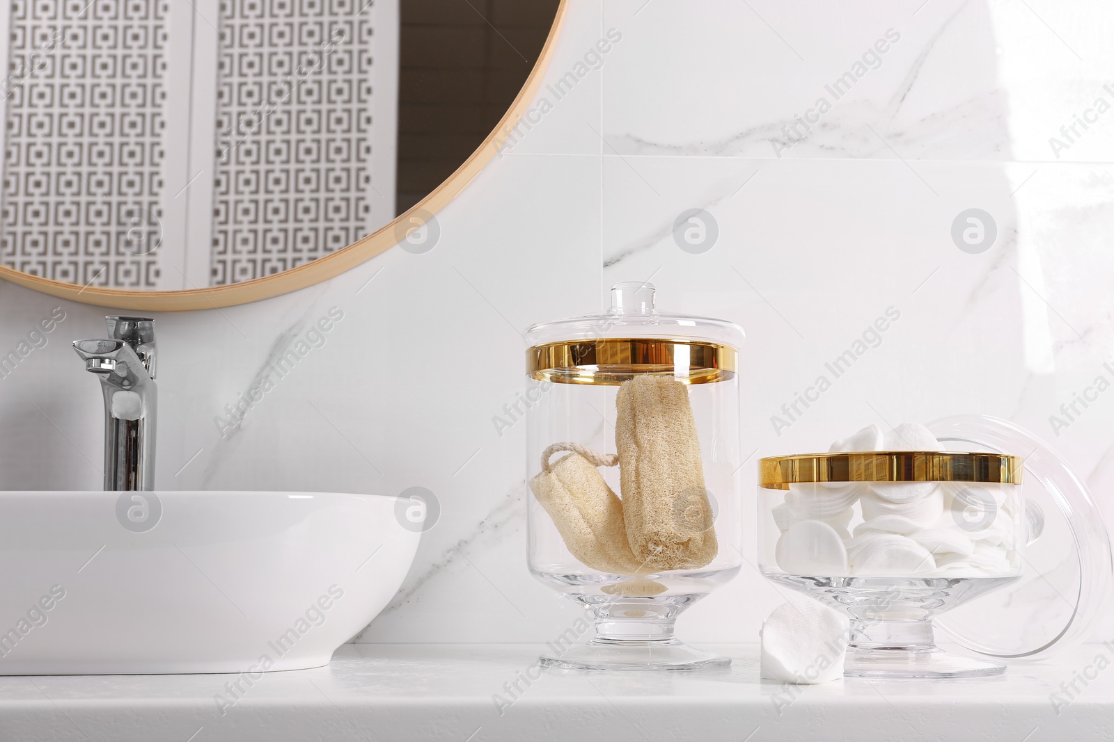Photo of Glass jars with cotton pads and loofahs on table in bathroom