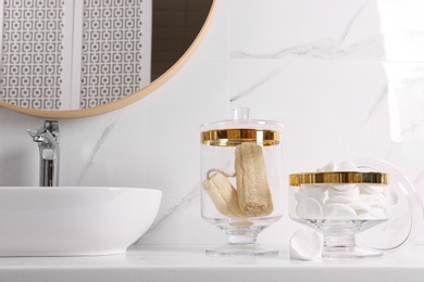 Photo of Glass jars with cotton pads and loofahs on table in bathroom