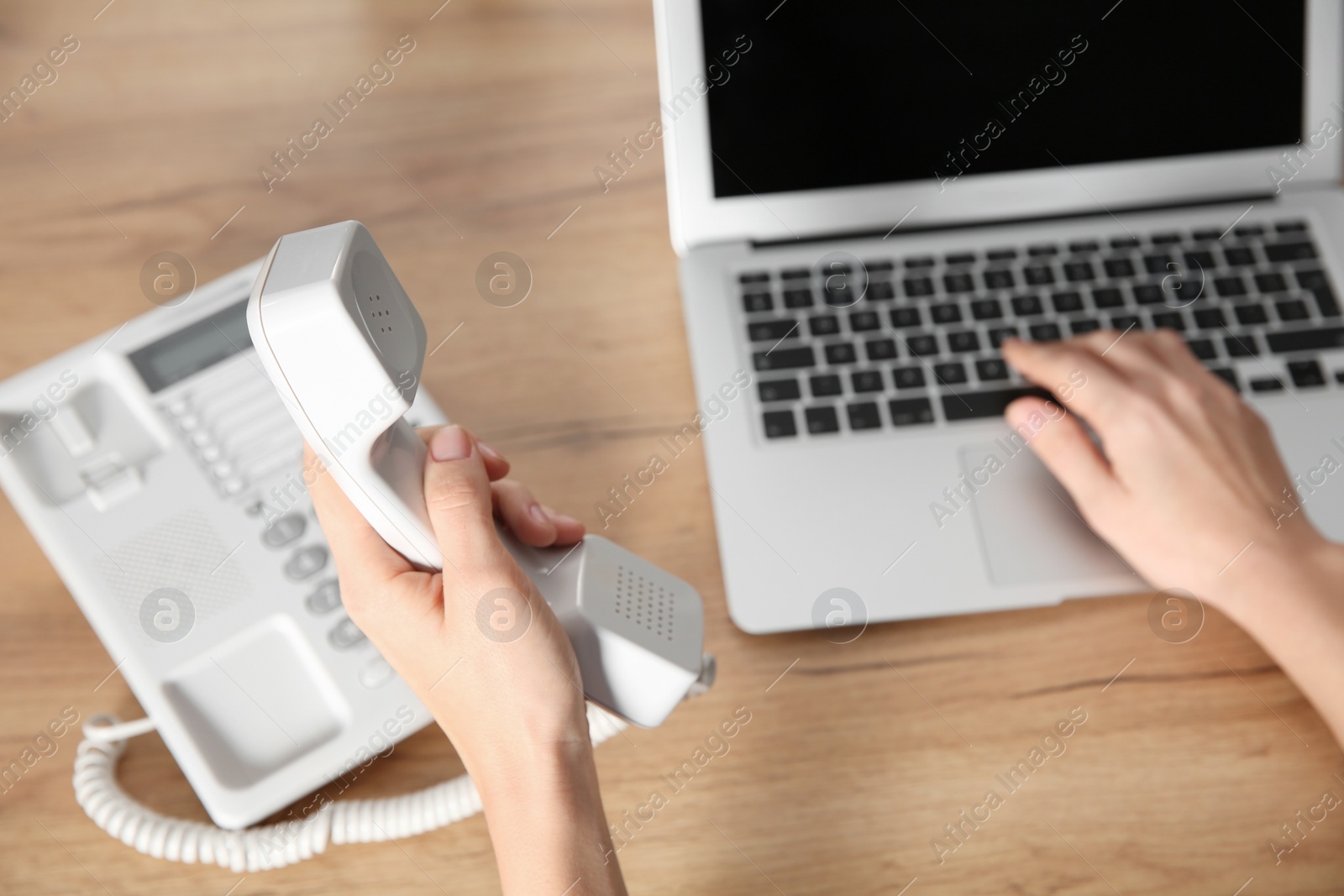 Photo of Female technical support operator with stationary phone at workplace, closeup of hands