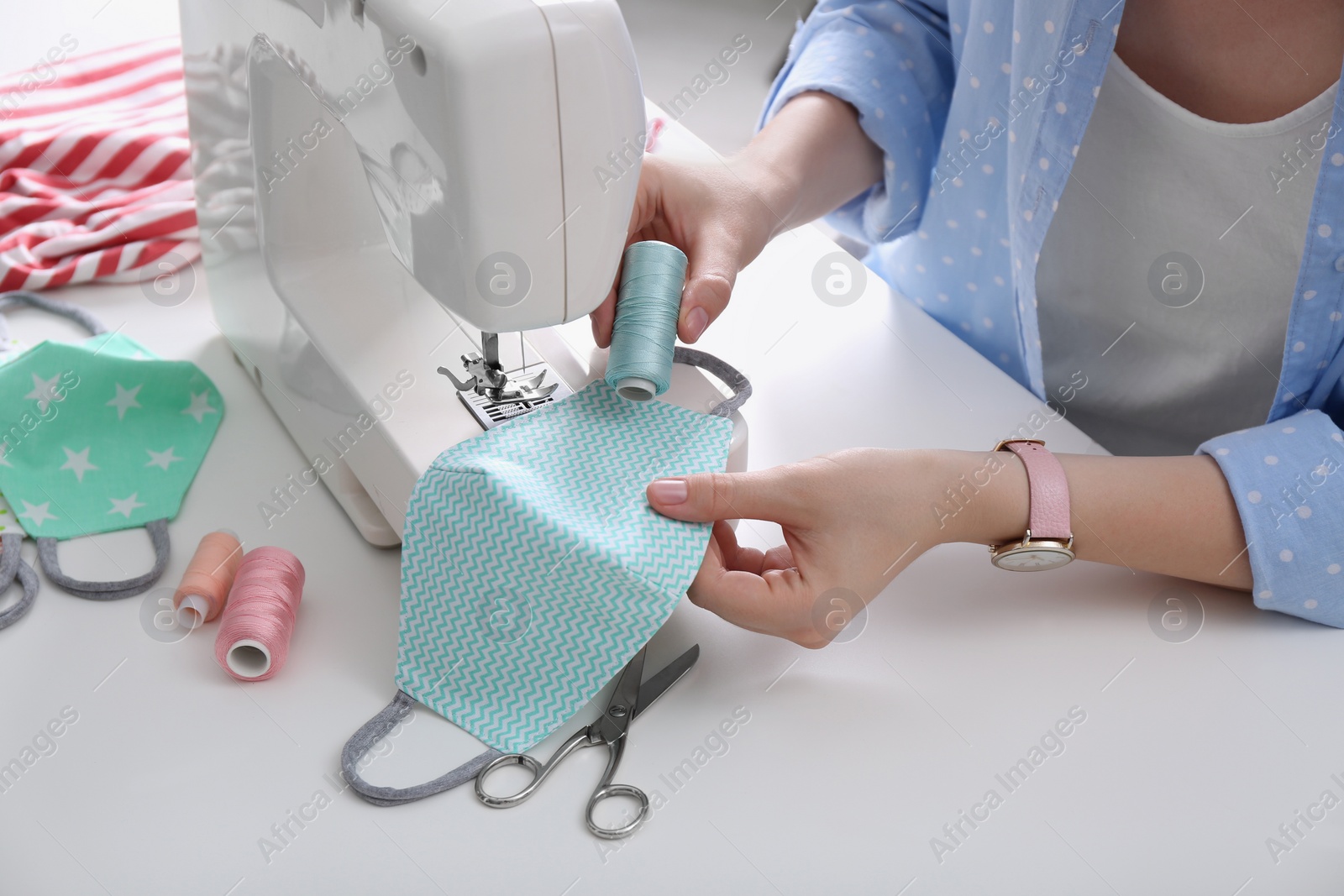 Photo of Woman making cloth mask with sewing machine at white table, closeup