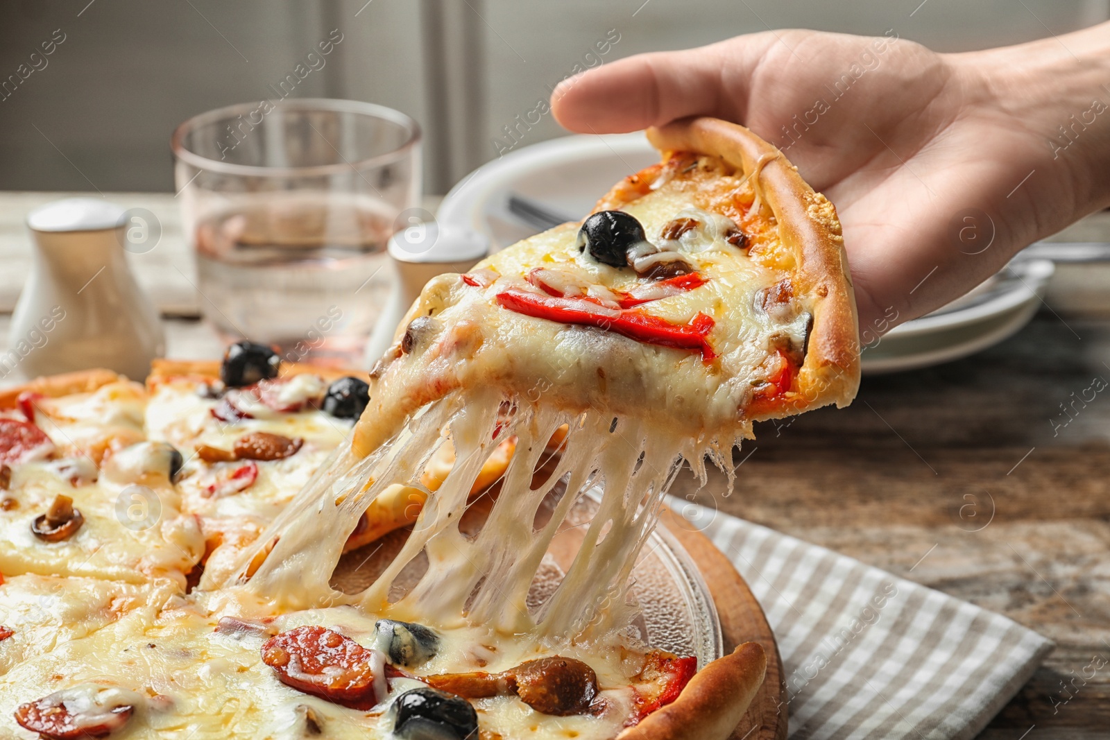 Photo of Woman holding slice of delicious hot pizza over table, closeup