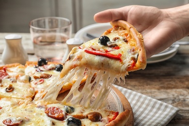 Woman holding slice of delicious hot pizza over table, closeup