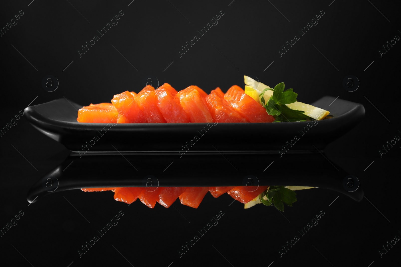 Photo of Delicious salmon sashimi served with lemon and parsley on black mirror surface