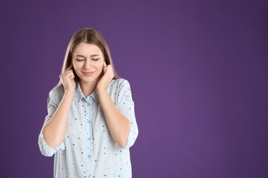 Photo of Emotional young woman covering her ears with fingers on purple background. Space for text