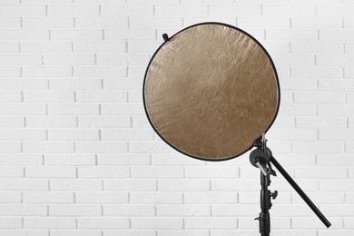 Photo of Professional golden reflector on tripod against white brick wall, space for text. Photography equipment