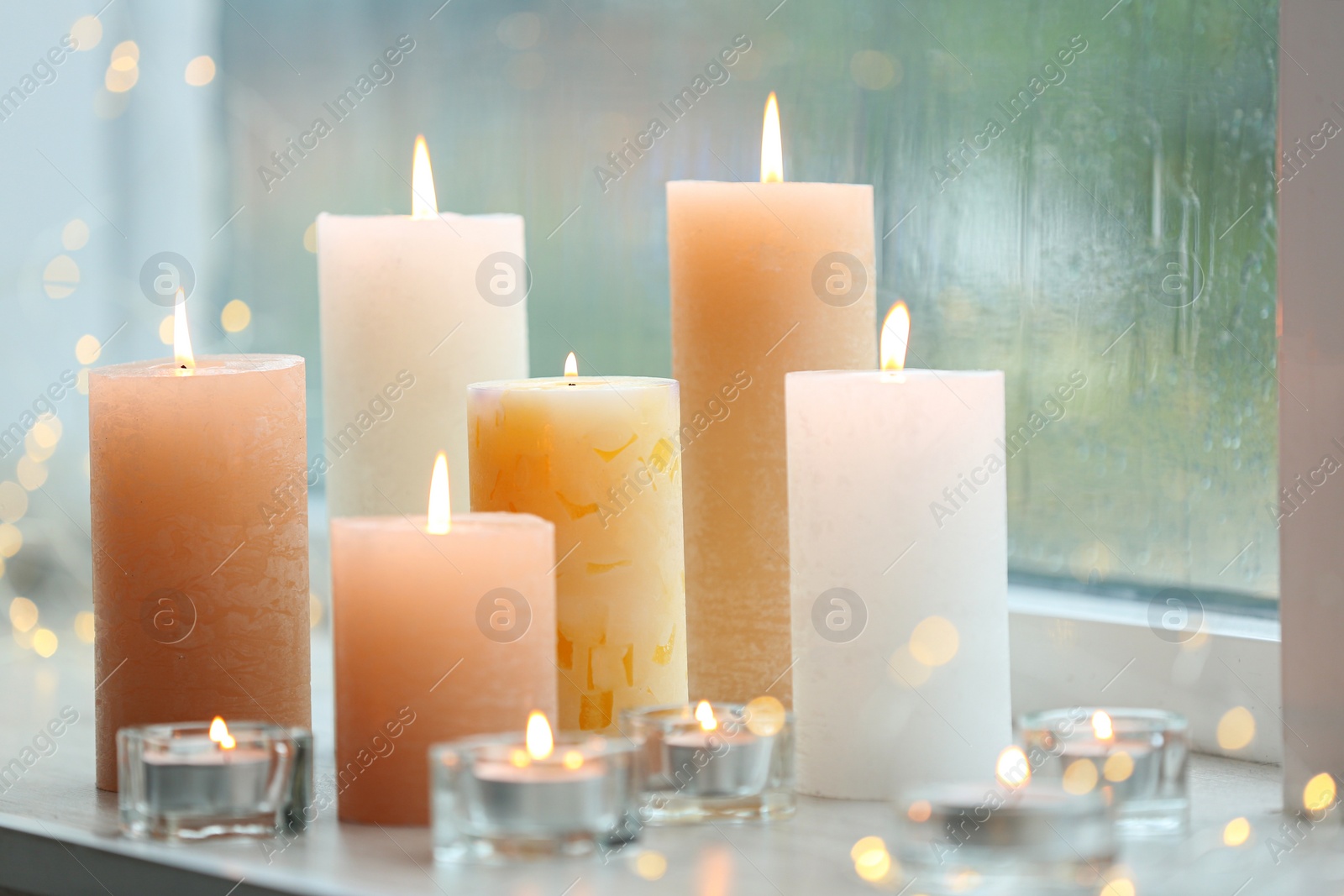 Photo of Beautiful burning candles and fairy lights at windowsill on rainy day