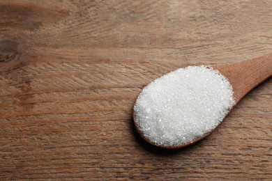 Spoon of white sugar on wooden table, closeup. Space for text