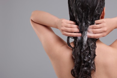 Photo of Woman washing hair on grey background, back view. Space for text