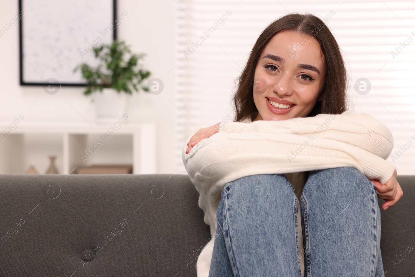 Photo of Beautiful young woman in stylish warm sweater on sofa at home, space for text