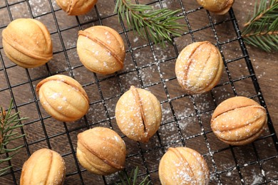 Photo of Delicious nut shaped cookies with powdered sugar and fir branches on wooden table, flat lay