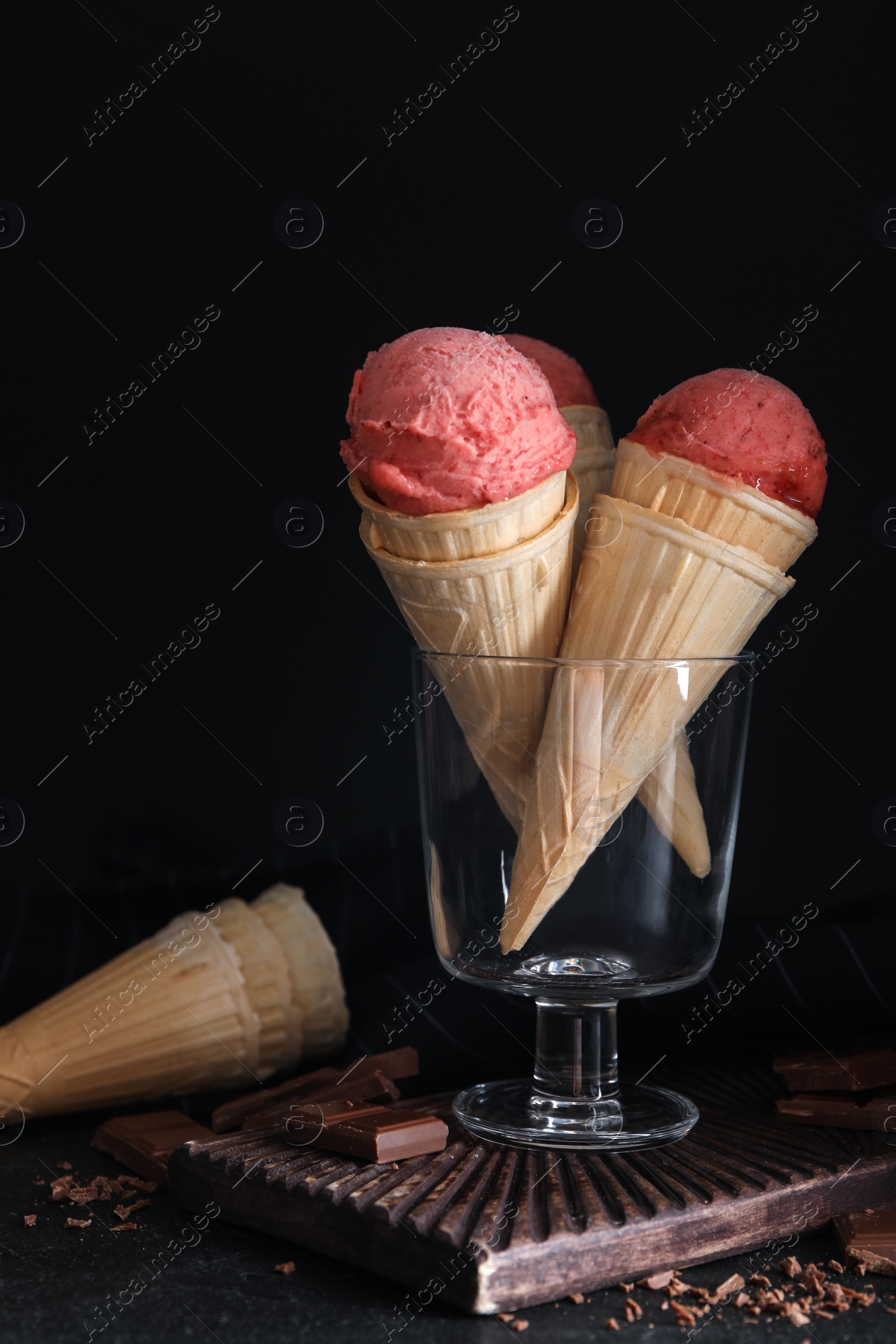 Photo of Delicious pink ice cream in wafer cones and chocolate on black table