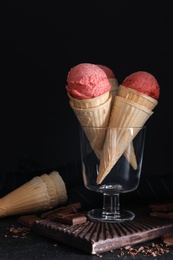 Delicious pink ice cream in wafer cones and chocolate on black table