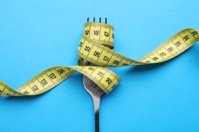 Fork with measuring tape on light blue background, top view. Diet concept