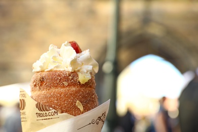 PRAGUE, CZECH REPUBLIC - APRIL 25, 2019: Traditional dessert trdelnik with whipped cream on city street, closeup. Space for text