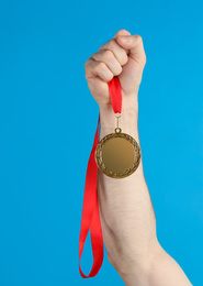 Photo of Man holding golden medal on blue background, closeup. Space for design