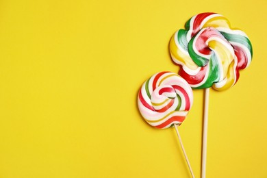 Photo of Sticks with different bright lollipops on yellow background, flat lay. Space for text