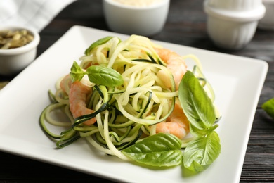 Photo of Delicious zucchini pasta with shrimps and basil on black wooden table, closeup