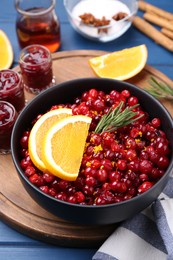 Cranberries in bowl, jars with sauce and ingredients on blue wooden table, closeup