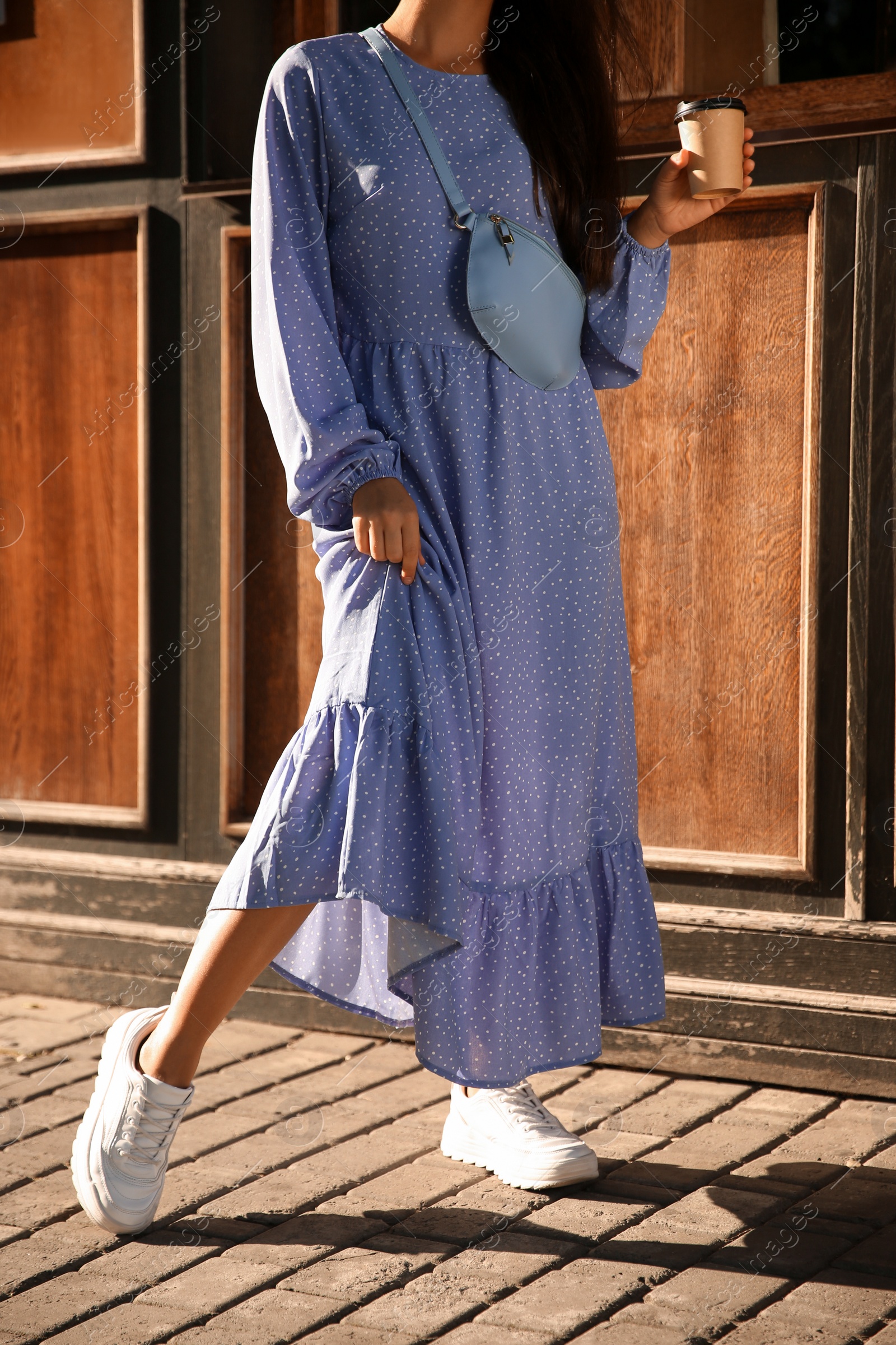 Photo of Woman in stylish blue dress with handbag and cup of coffee near wooden building outdoors, closeup