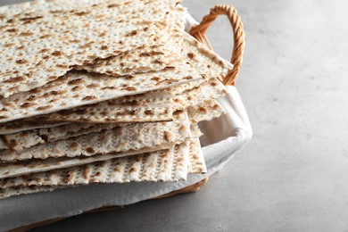 Photo of Traditional matzos in basket on light grey table, closeup