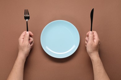 Photo of Man with cutlery and empty plate at brown table, top view
