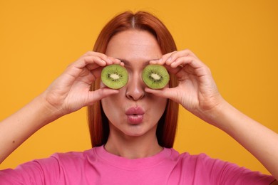 Photo of Funny woman covering eyes with halves of fresh kiwi on orange background