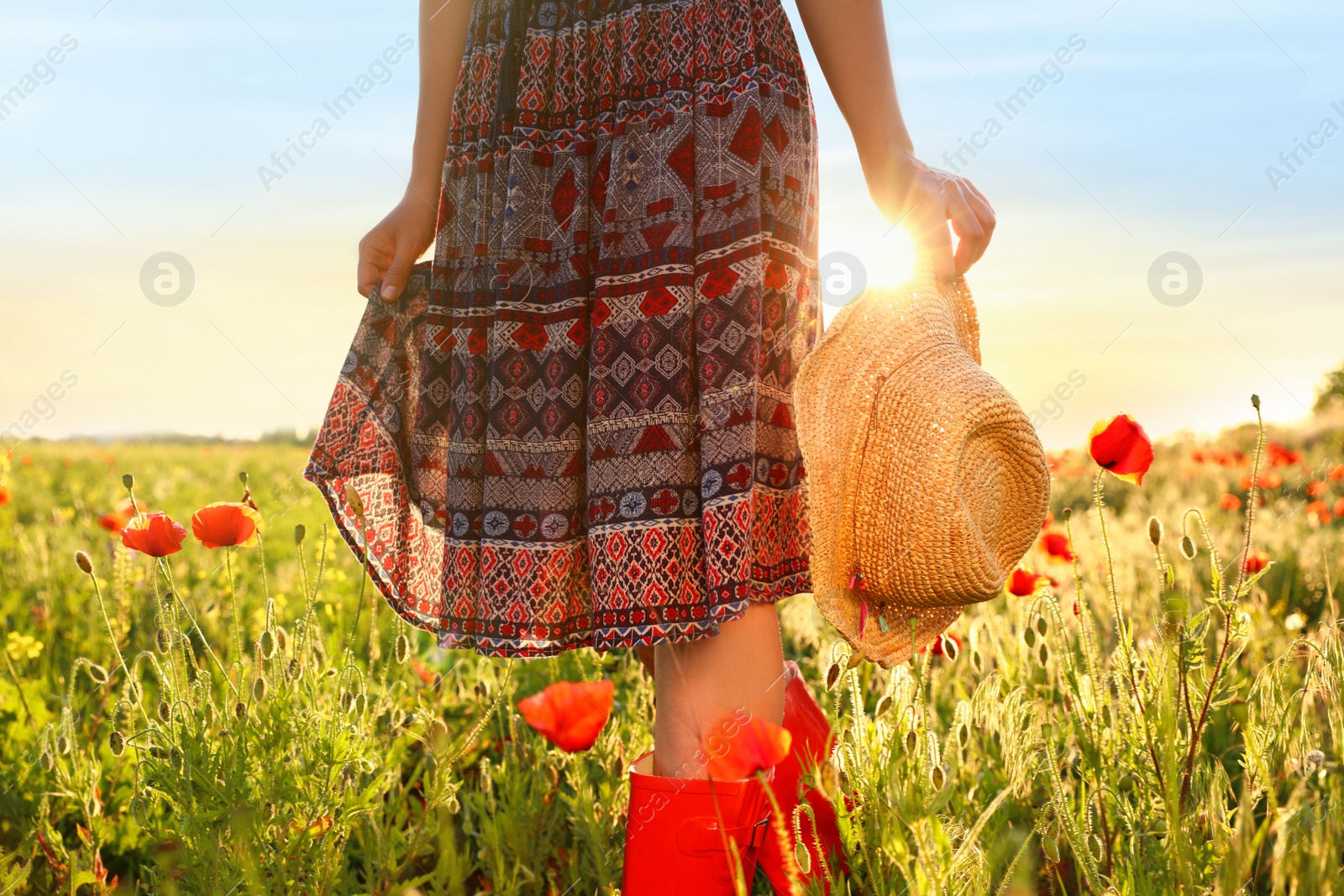 Photo of Woman wearing red boots in poppy field on sunny evening, closeup