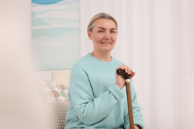 Photo of Senior woman with walking cane sitting on sofa at home