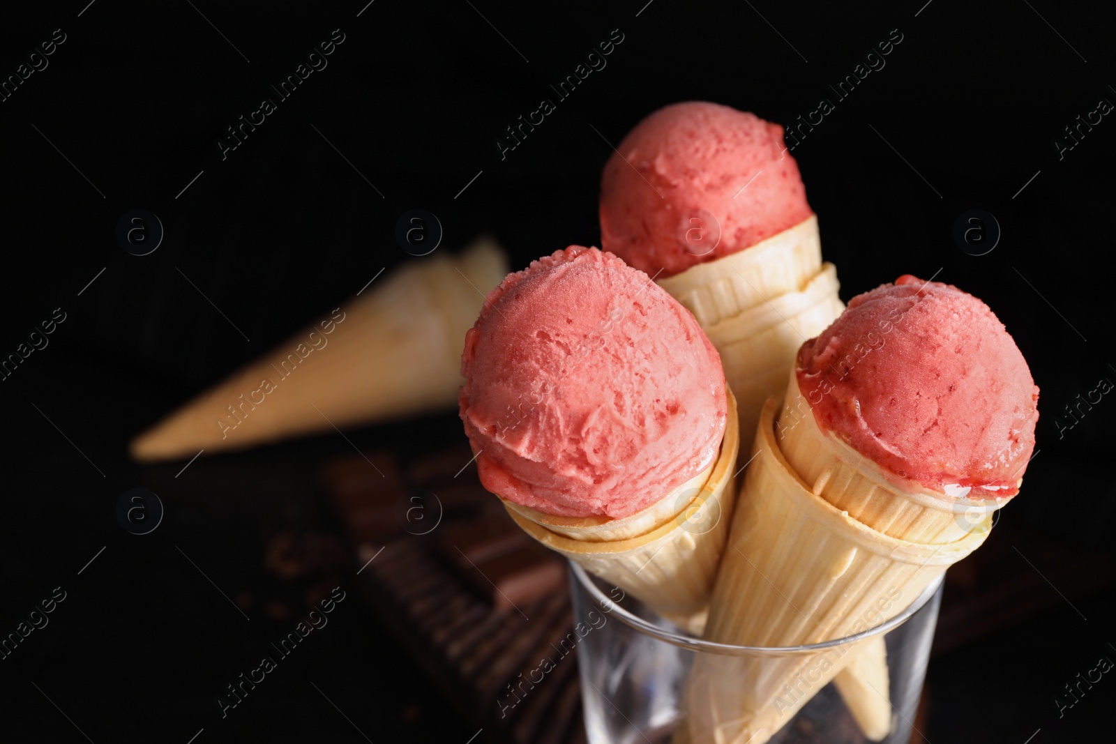 Photo of Delicious pink ice cream in wafer cones on black background, closeup. Space for text